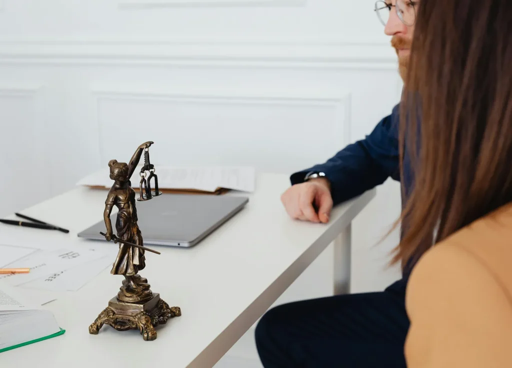 A bronze Lady Justice statue on a desk between two people in a professional meeting, representing the transition from legal conflict to a mediated discussion.